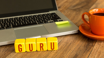 Guru written on a wooden cube in front of a laptop