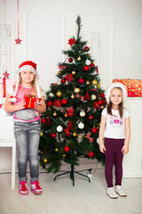 Two girls in Christmas costumes stand beside the tree with gifts