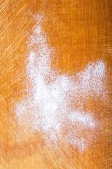 White wheat flour is scattered on an old worn cutting board. Bac