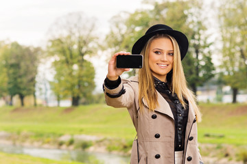 Beautiful teenage girl taking a selfie in autumn in park