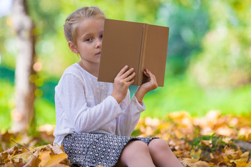 Adorable little girl reading a book in beautiful autumn park 