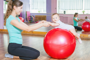 Mother with happy baby doing exercises with gymnastic ball