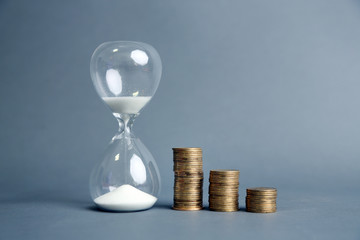 Hourglass with coins on gray background