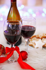 Bottle and glasses of wine with Christmas decor against colorful bokeh lights background