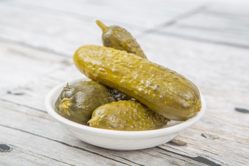 Dill pickles in a white bowl over wooden background