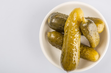 Dill pickles in a white bowl over white background