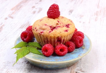 Fresh baked cupcake and raspberries on plate on old wooden background, delicious dessert
