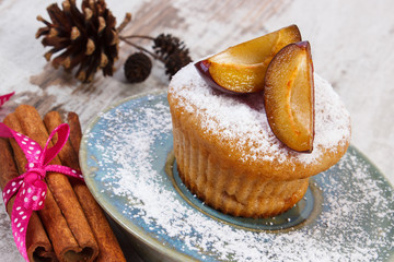 Muffins with plums and powdered sugar, cinnamon sticks on old wooden background, delicious dessert