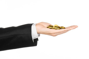 Fototapeta premium Money and business topic: hand in a black suit holding a pile of gold coins in the studio on a white background isolated