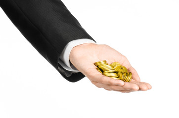 Fototapeta premium Money and business topic: hand in a black suit holding a pile of gold coins in the studio on a white background isolated