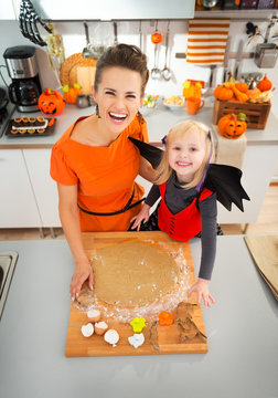 Mother With Daughter In Bat Costume Making Halloween Cookies