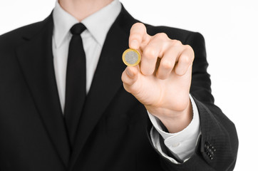 Money and business theme: a man in a black suit holding a coin 1 Euro in the studio on a white...