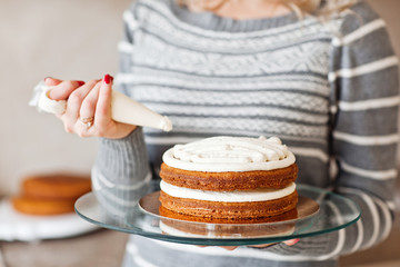 Young beautiful blond woman in winter dress making cake with cre