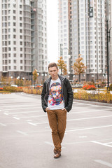 Handsome brown-haired young man in autumn black jacket and white t-shirt with his portrait is walking. Outdoor fashion male portrait.