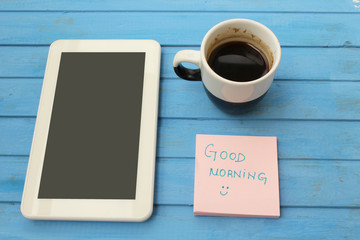 Touch screen tablet computer, cup of coffee, sticky note with good morning message - on blue background