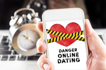 Hand holding mobile with caution tape on heart and Danger online