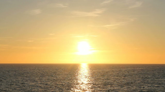 The bright sun is setting over water with gentle waves