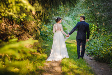 Bride and groom walking in park on wedding day. 