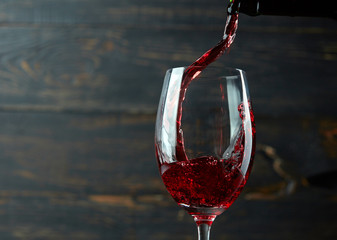 Pouring red wine into the glass against dark wooden background