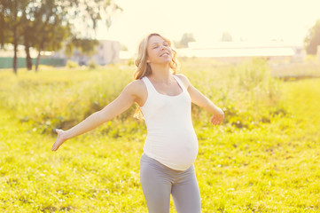 Naklejka na ściany i meble Happy beautiful smiling pregnant woman enjoys warm sunny summer