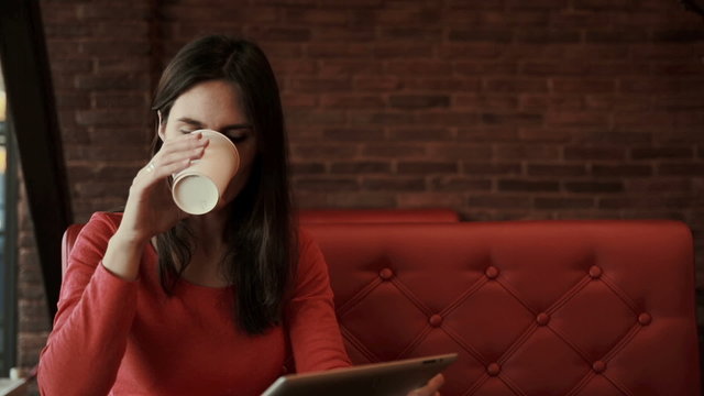 woman using tablet drinking coffee and smiling in cafe