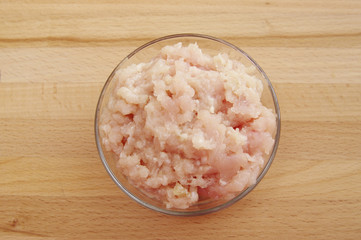 Fototapeta na wymiar Raw minced chicken meat in transparent round cup on wooden background, top view