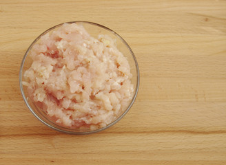 Raw minced chicken meat in transparent round cup on wooden background, top view