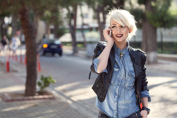 portrait of a young punk style blond woman outdoor, talking with her mobile phone