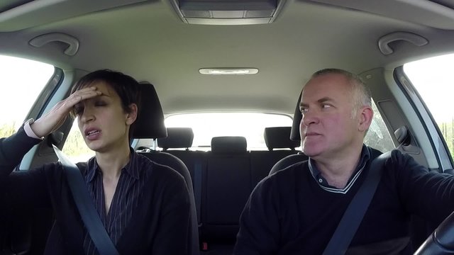 Married caucasian couple on road trip, people traveling by car on the street, man driving vehicle with ill woman having headache, migraine. Husband talking to sick wife with nausea for motion sickness