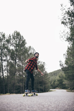 Man riding on a longboard skate on a road through a forest