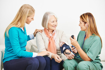Enkelin beruhigt Seniorin beim Blutdruck messen