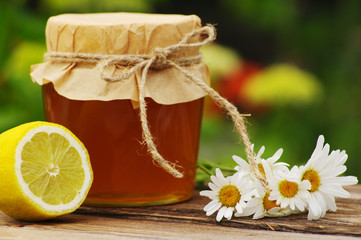 Obraz na płótnie Canvas Honey in a glass jar, camomile flowers, a lemon in a summer sunny day. Honey with flowers and lemon