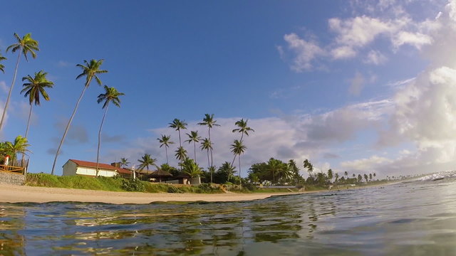Tropical beach coast with palm and sand in summertime. Underwater camera view from a wave