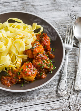Chicken meatballs in tomato sauce and fettuccine pasta in a brown bowl on bright wooden surface.