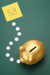 House savings - golden piggy bank, coins and a house sketch