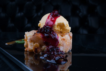 Apple pie served on black plate with ice cream and fruit jam. Ice cream has vanilla flavor. 