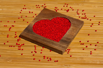 Heart from red beads in wooden heart-shaped box on the background of bamboo
