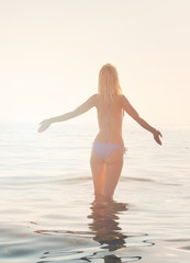 Young woman raising her hands and enjoying sunrise on the beach near sea, ocean. Freedom concept, sea, sun, summer, holiday, vacation.