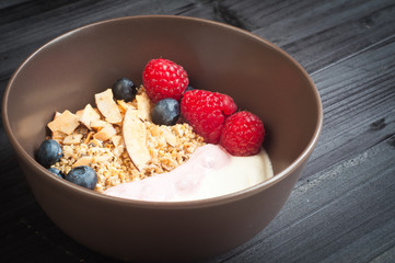 A bowl of healthy breakfast fruit muesli with yogurt and topped with fresh strawberries, sliced melon, goji berries, blueberries and coconut shavings.