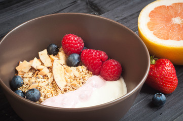A bowl of healthy breakfast fruit muesli with yogurt and topped with fresh strawberries, sliced melon, goji berries, blueberries and coconut shavings.