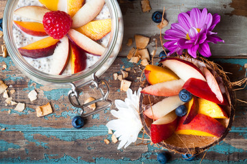 Homemade oats with sliced peaches and berries with a coconut shell on a rustic wooden table.