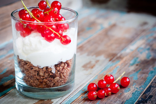 Healthy breakfast of crunchy granola with yogurt and topped with fresh red berries. Served in layers in a glass on a rustic wooden table.