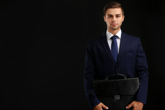 Elegant man in suit with briefcase on dark background