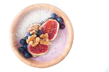 Fototapeta na wymiar Healthy breakfast berry smoothie bowl of blueberry and strawberry blended with kefir yogurt and topped with fresh fig, blueberries, walnuts and coconut. Served in a wooden bowl isolated on white.