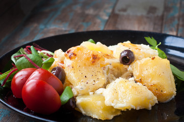 Bacalhau com natas. A Portuguese Brazilian dish of salt cod cooked with potatoes, cream and olives. Served with tomatoes and fresh salad leaves.