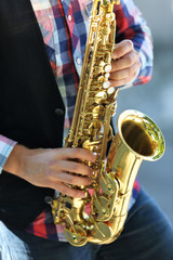 Handsome young man plays sax outdoors, close up
