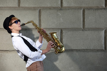 Fototapeta na wymiar Attractive woman in hat plays saxophone on brick wall background