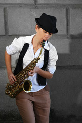 Naklejka premium Attractive woman in hat plays saxophone on brick wall background