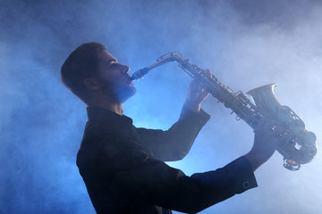 Elegant saxophonist plays jazz  in blue smoke