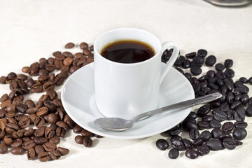 Cup of coffee beside natural roasted and torrefacto coffee beans, on white table